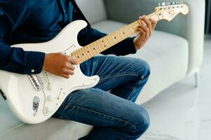 gitarrist spelar gitarr på soffa på Hem praktiserande gitarr på Hem koppla av förbi spelar strängad instrument. foto