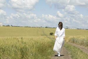 en kvinna i en vit klänning stående i en fält foto