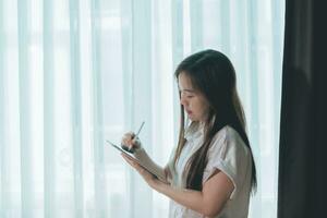 asiatisk kvinna använder sig av läsplatta pc i levande rum på Hem, företag begrepp. foto