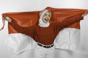 Lycklig leende indonesiska muslim kvinna bär röd topp och vit hijab innehav Indonesiens flagga till fira indonesien oberoende dag. isolerat förbi vit bakgrund. foto