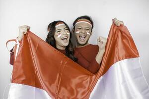 en ung asiatisk par med en Lycklig framgångsrik uttryck bär röd topp och pannband medan innehav Indonesiens flagga, isolerat förbi vit bakgrund. Indonesiens oberoende dag begrepp. foto