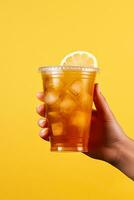 en hand innehav hämtmat plast kopp av utsökt iced citron- te isolerat på gul bakgrund. ai genererad foto