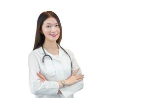 professionell ung ålder asiatisk kvinna läkare stående leende i Bra humör med vapen korsade i kontor rum i sjukhus medan arbetssätt isolerat på vit bakgrund. bär vit morgonrock och stetoskop. foto