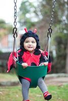 liten bebis flicka bär en nyckelpiga kostym Sammanträde på en litet barn gunga. halloween begrepp. foto