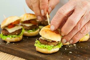 sätta på en tandpetare på hamburgare. steg förbi steg förberedelse av mini hamburgare. hemlagad mini hamburgare för barn eller aptitretare. små hamburgare. montering hamburgare foto