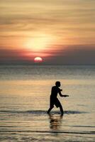 man spelar flygande maträtt på hav beac mot skön solnedgång himmel på reser destination foto