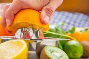 förberedelse av orange druva eller multivitamin juice, händer pressa juice på en manuell metall juicepress omgiven förbi färsk tropisk frukt foto