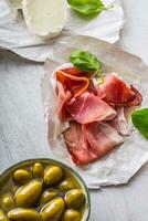 skinka oliver oliv olja mozzarella ost tomater basilika - Ingredienser italiensk eller medelhavs kök. foto