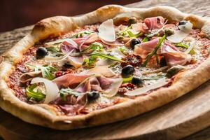 italiensk pizza med skinka tomater oliver oliv olja parmesan ost och ruccola. foto