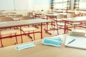 ansikte mask på en lärare och skola skrivbord i en skola klassrum foto