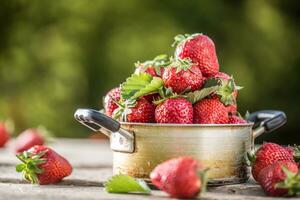färsk mogen jordgubbar i årgång kök pott på gammal trädgård tabell foto