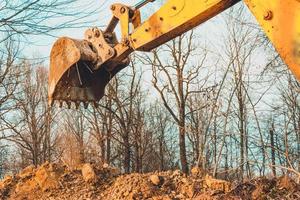 grävmaskinen utför grävarbeten genom att gräva marken med en hink i skogen.