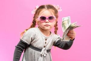 liten flicka i glas med ett paket och pengar på en rosa bakgrund, barn och shopping. foto