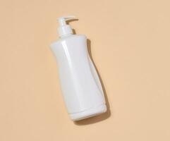 vit plast behållare med en pump för flytande Produkter på en beige bakgrund. behållare för kosmetika, tvål, grädde foto