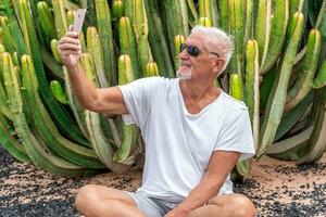 stilig medelålders man tar en selfie i främre av en stor kaktus i ett exotisk havet tillflykt foto