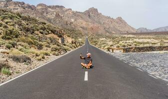 mitten åldrig man turist tar en selfie Sammanträde i de mitten av ett asfalt väg i de bergen foto