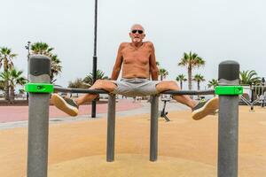 attraktiv pensionerad man håller på med gymnastiska övningar i ett utomhus- offentlig Gym på en tillflykt foto