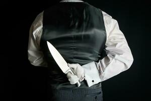 butler eller servitör i svart väst eller väst innehav skarp kniv Bakom hans tillbaka. begrepp av butler gjorde Det. klassisk mörda mysterium. foto