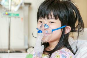 sjuk liten asiatisk flicka inandning med nebulisator för respiratorisk behandling foto