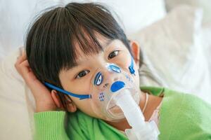 sjuk liten asiatisk flicka inandning med nebulisator för respiratorisk behandling foto