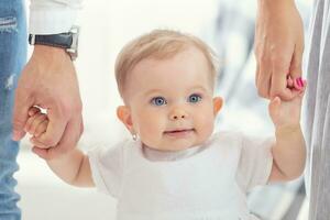 oskyldig se av en blåögd bebis flicka innehav mamma och pappas händer foto