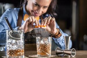 bartender pressar orange in i ett gammal fashioned cocktail med whisky i ett dekorativ glas foto
