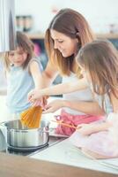 mamma med två ung tvillingar döttrar i de kök matlagning spaghetti foto