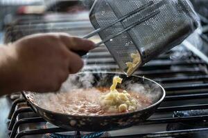 kock sätta Gnocchi in i en sås på en gas sparken spis foto