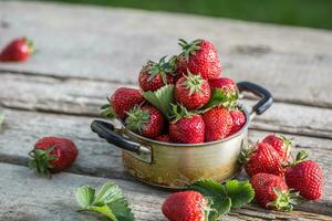 färsk mogen jordgubbar i årgång kök pott på gammal trädgård tabell foto