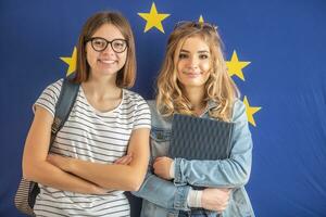 två Tonårs flicka studenter stå i främre av teh flagga av europeisk union foto