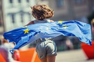 eu flagga. söt Lycklig flicka med de flagga av de europeisk union. ung Tonårs flicka vinka med de europeisk union flagga i de stad foto