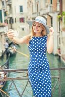 skön gir resande turist i blå polka punkt klänning göra selfie i Venedig Italien. attraktiv blond mode modell ung kvinna foto