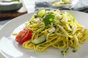 spaghetti zucchini rå vegan pasta med fetaost ost gurka och basilika foto