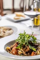 detalj av kött linguine med tomater och raket eras med vin på en cafeteria tabell foto