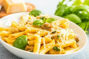 pasta penne med kyckling bitar svamp basilika parmesan ost och vit vin. italiensk mat i vit tallrik på kök tabell foto