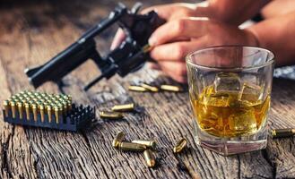 man händer innehav pistol och alkohol glas på de tabell foto