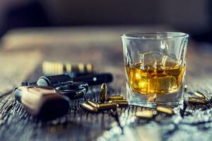 glas av whisky cognac eller bourbon med revolver och kulor på trä- tabell foto