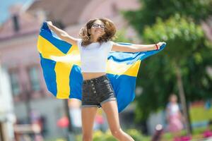 Lycklig flicka turist gående i de gata med Sverige flagga foto