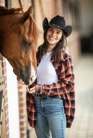 cowgirl med en stor leende matar henne häst från de hand inuti de stabil foto