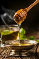 honung. honung och honung dipper på rustik ek tabell. varm ört te i de bakgrund foto