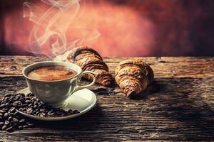 kaffe. kopp av kaffe croissanter och kaffe bönor. årgång kopp och gammal ek tabell foto
