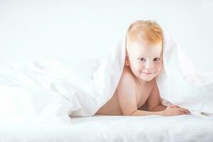 habby ung smilling barn pojke i vit säng foto