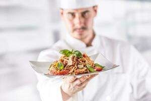 kock i restaurang kök innehav tallrik med italiensk måltid spaghetti bolognese foto