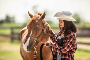 skön flicka i en hatt och rutig skjorta samtal till lugna en måla häst ut i en ranch foto