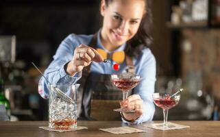 leende bartender bär trä- rosett slips dekorerar manhattan cocktail dryck med en körsbär foto