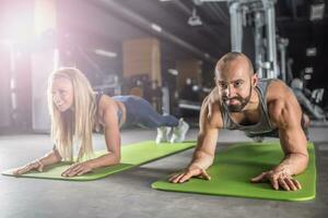 sport par håller på med planka övning träna i kondition centrum. man och kvinna praktiserande planka i de Gym foto