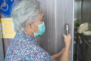 asiatisk senior eller äldre gammal damkvinna som bär en ansiktsmask öppnar toalettdörren för funktionshindrade för att skydda säkerhetsinfektion covid-19 coronavirus. foto