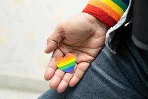 asiatisk dam som bär blå jeanjacka eller jeansskjorta och håller regnbågens färgflagghjärta, symbol för HBT stolthet månad firar årliga i juni sociala av homosexuella, lesbiska, bisexuella, transpersoner, mänskliga rättigheter. foto