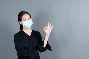 ung asiatisk kvinna som bär medicinsk ansiktsmask och visar ok tecken foto