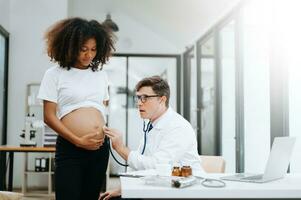 gravid afrikansk kvinna har utnämning med läkare på klinik. manlig gynekolog ob gyn läkare specialist med stetoskop lyssnar till bebis hjärtslag i mors mage. graviditet, hälsa vård foto